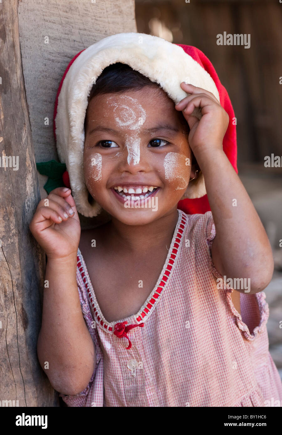 Myanmar, Burma, Mrauk U. Young village girl wearing a Christmas hat, her face decorated with thanaka, a local sun cream made Stock Photo