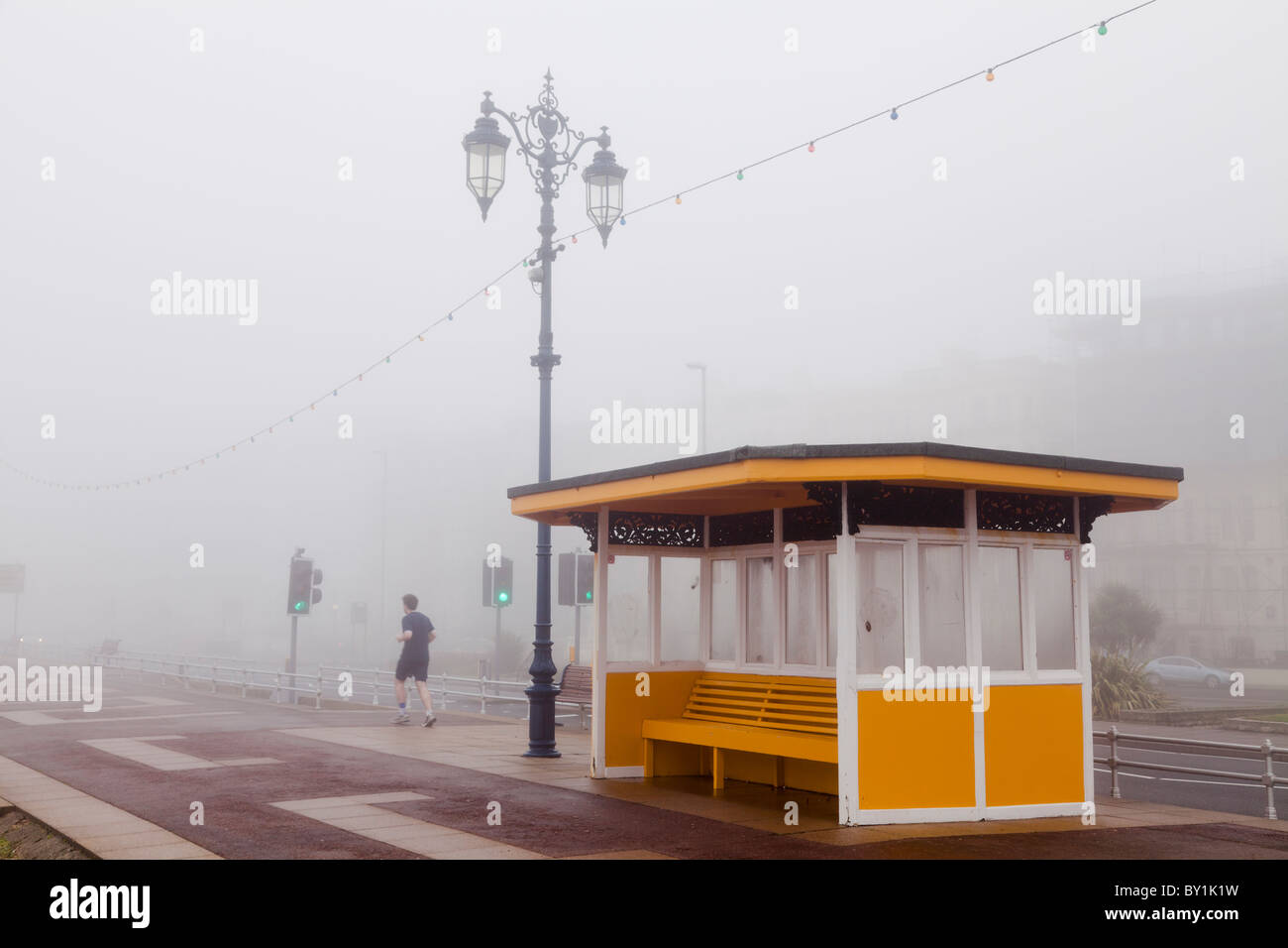 jogging in the fog on the seafront promenade in winter past a shelter