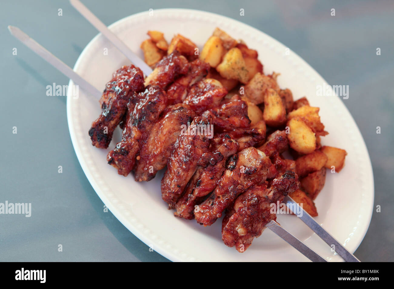 BBQ chicken wings on a skewer served with baked potatoes Stock Photo