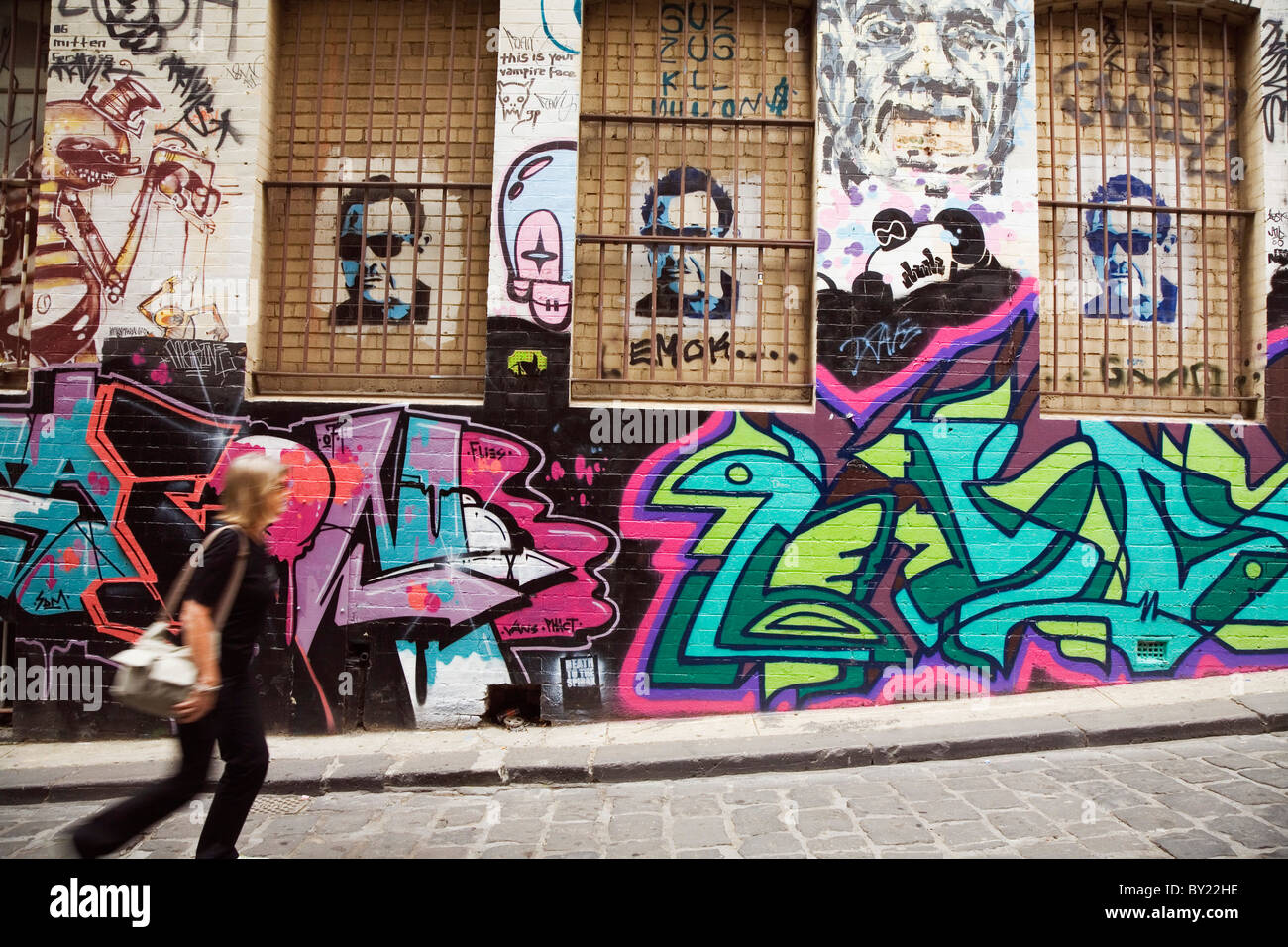Australia, Victoria, Melbourne.  A woman walks past colourful street art in Hosier Lane. Stock Photo