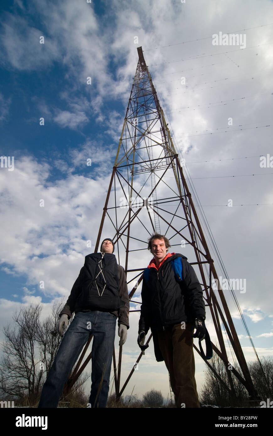 Two men posing in front of a radio antenna just before climbing up for