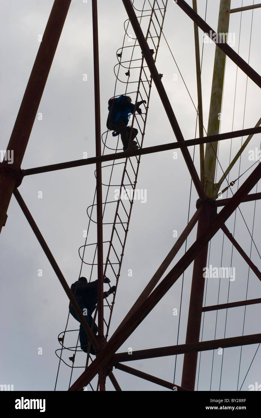 Two men climbing up a metal ladder of an radio antenna, going for a