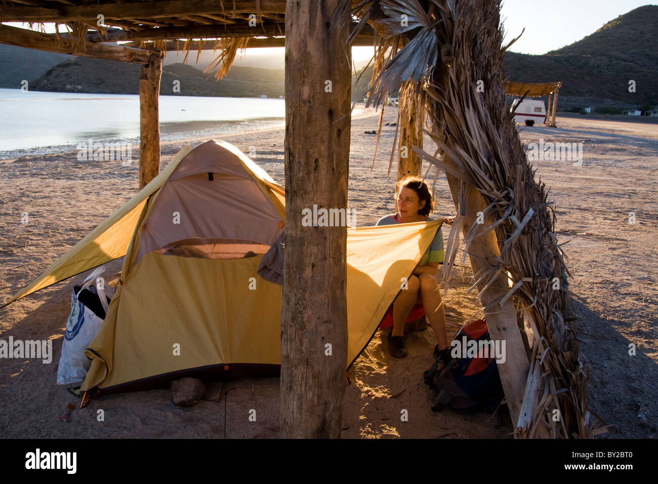A mature woman camps under a palapa on Playa Santispac, Baja California, Mexico. Stock Photo