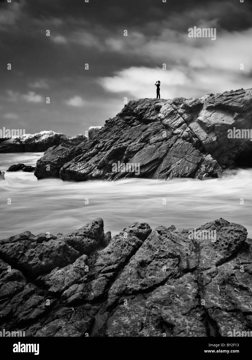 Woman standing on rocks with binoculars, looking out over the ocean. Malibu Beach, California. Stock Photo