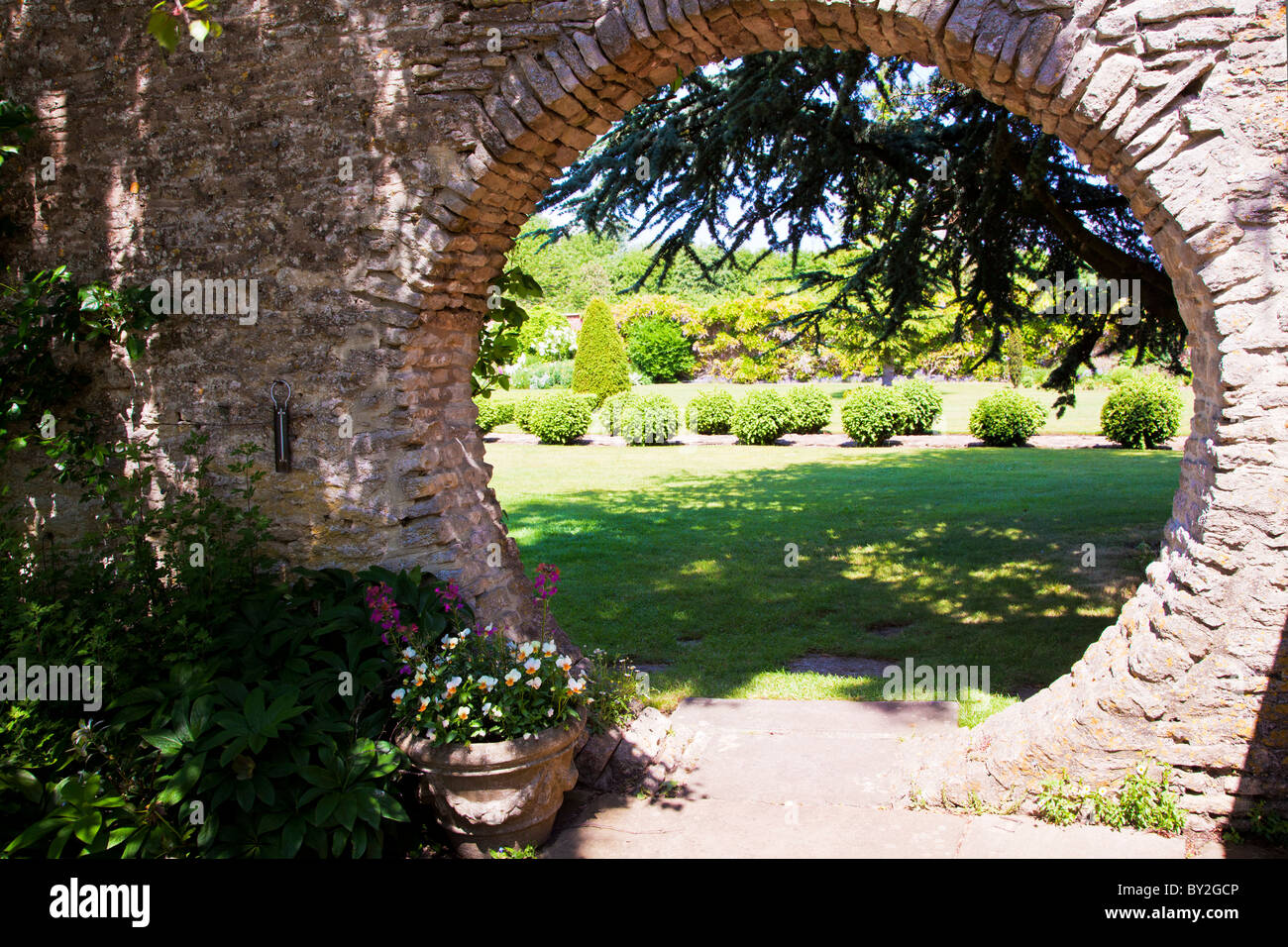 A circular opening in the wall of an English country summer garden with a view to the landscaped lawn and topiary beyond Stock Photo
