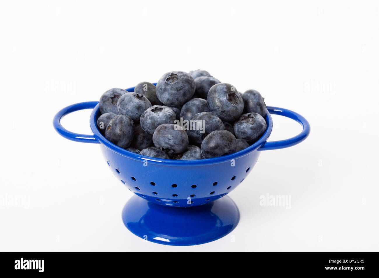 A small blue colander filled with fresh blueberries Stock Photo