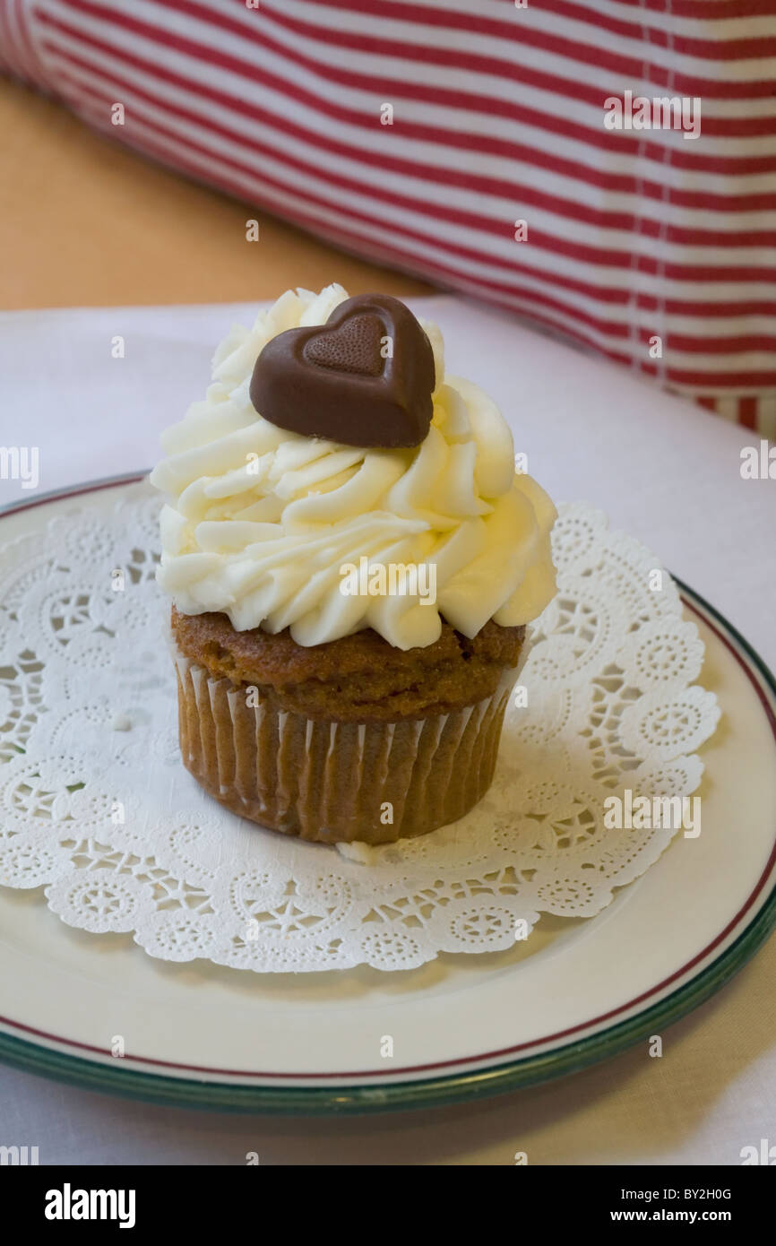 A cupcake piled high with butter icing and with a chocolate heart on top Stock Photo