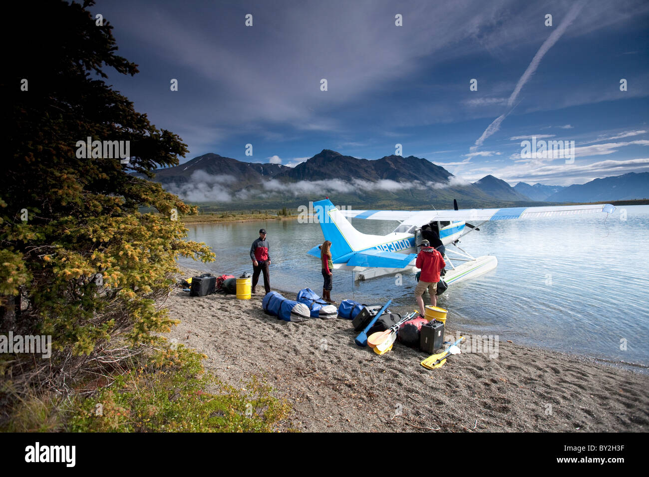 Two men and one woman unload gear from a plane on a lake in Alaska. Stock Photo