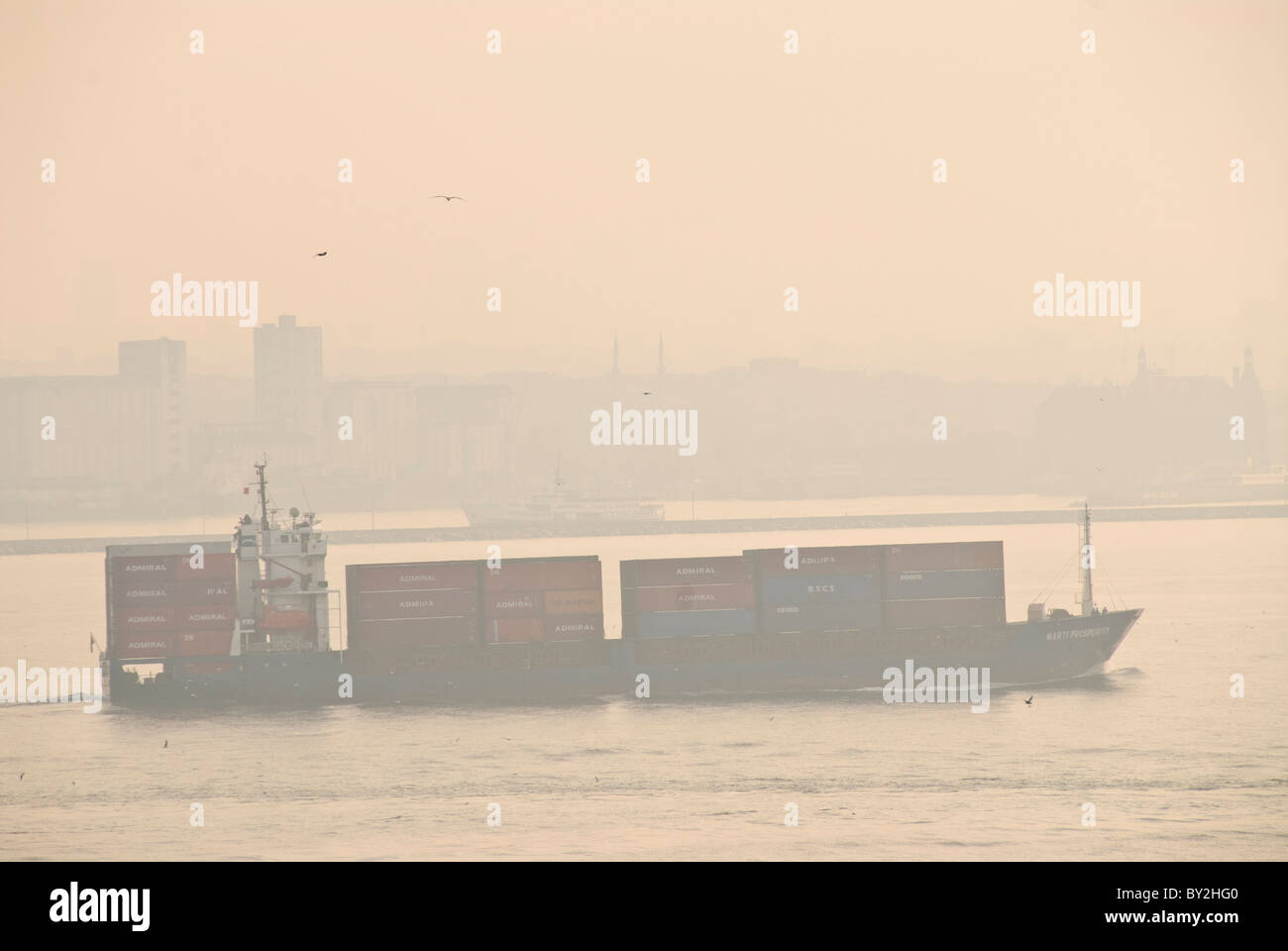 A large cargo ship passes through the narrow intersection of the Sea of Marmara, the Golden Horn, and the Bosphorus Strait, passing very close to shore in Istanbul, Turkey. Stock Photo