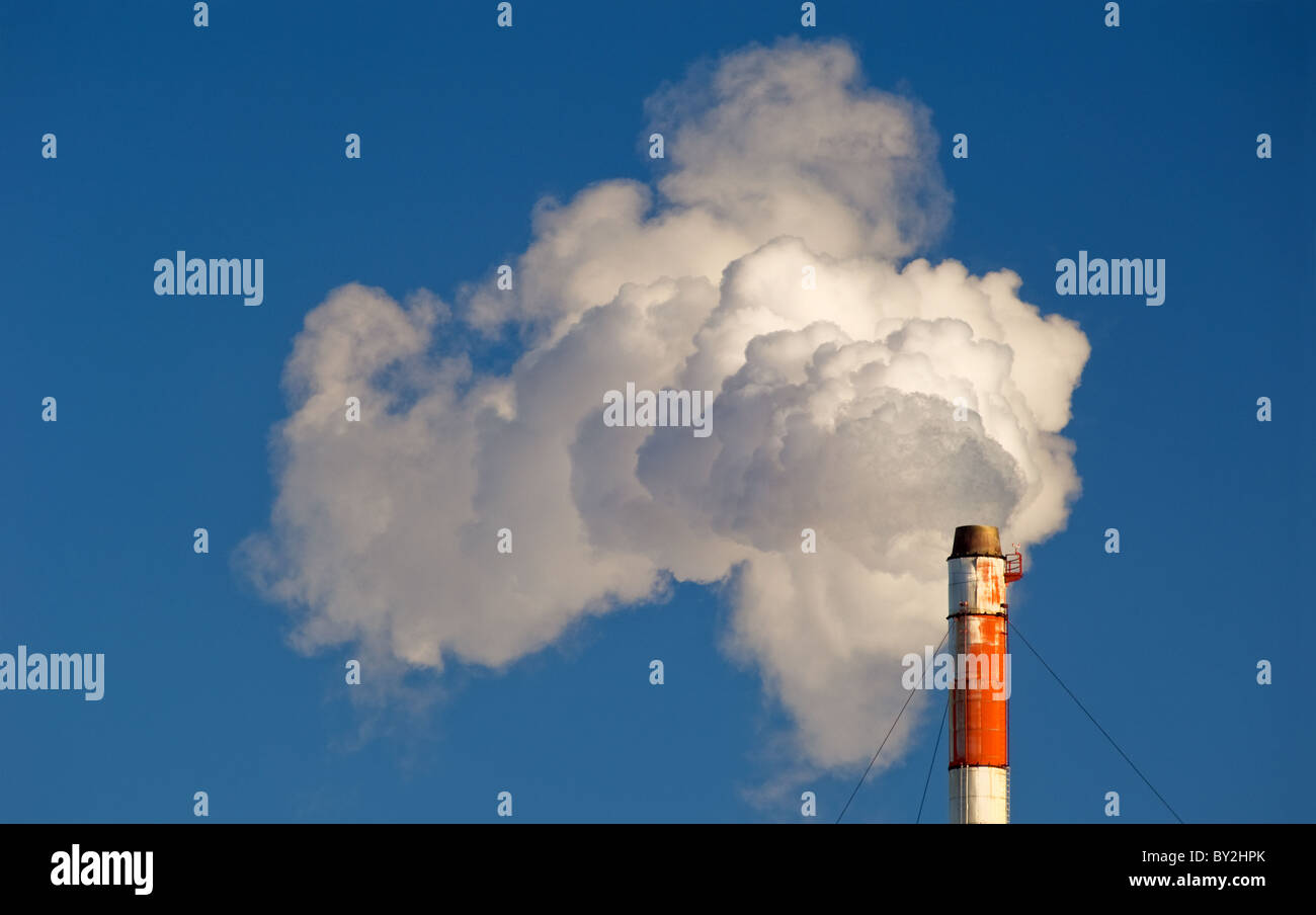 Smoke, gas and steam billows from a smokestack against a blue sky. Stock Photo