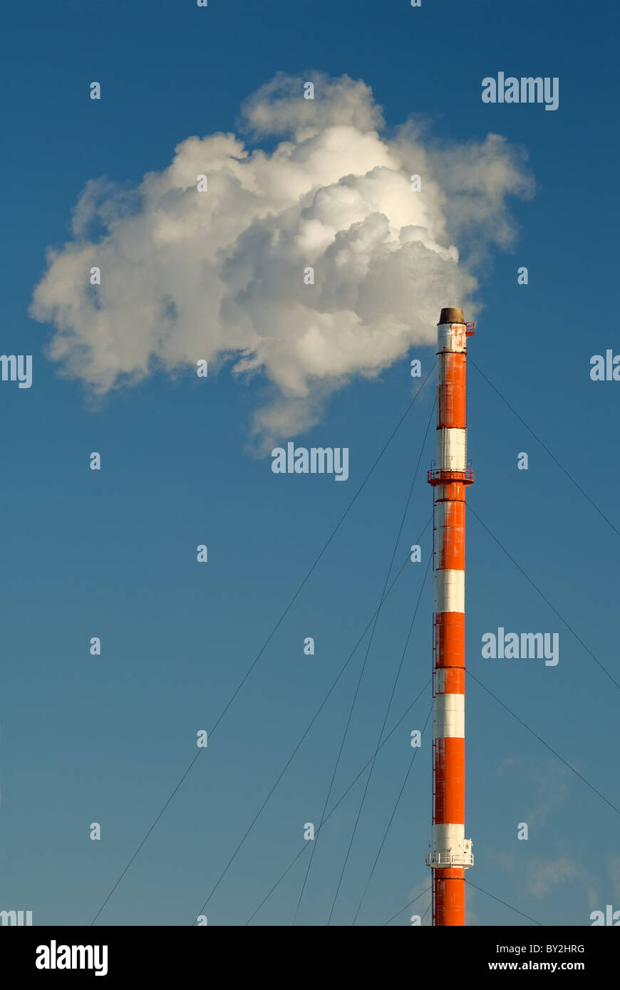 Smoke, gas and steam billows from a smokestack against a blue sky. Stock Photo