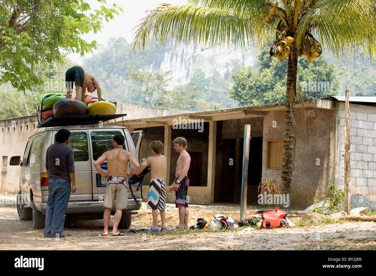 Kayakers unloading kayaks under palm trees next to a run down farmhouse in Mexico. Stock Photo