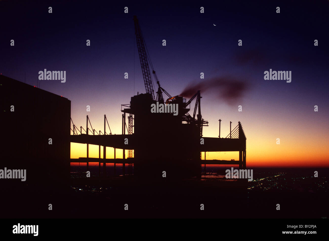 Crane on top of high rise commercial construction site at dusk with