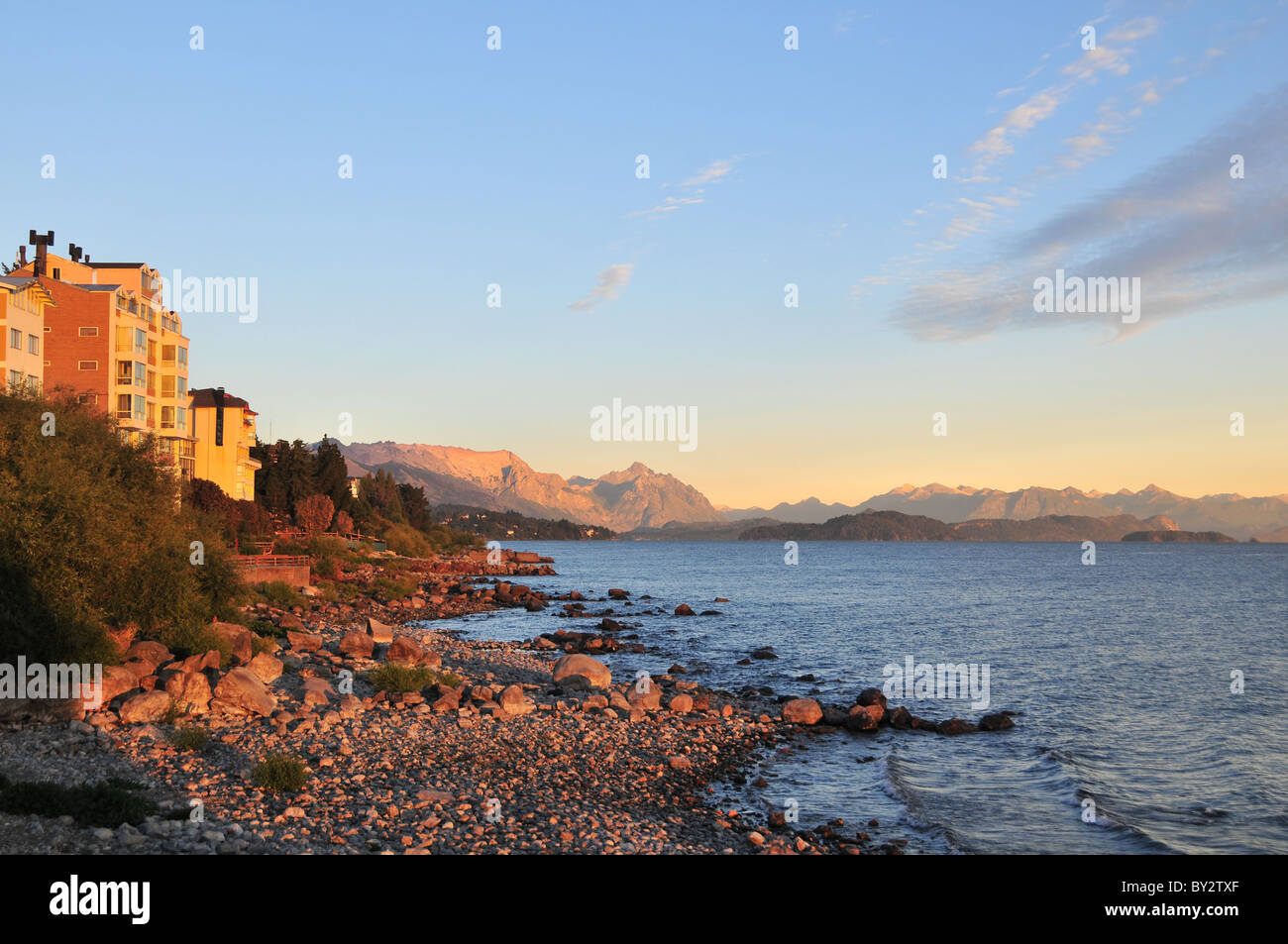 Stony beach view of morning waters of Lake Nahuel Huapi towards red sun glow Cerro Lopez and Andean peaks, Bariloche, Argentina Stock Photo