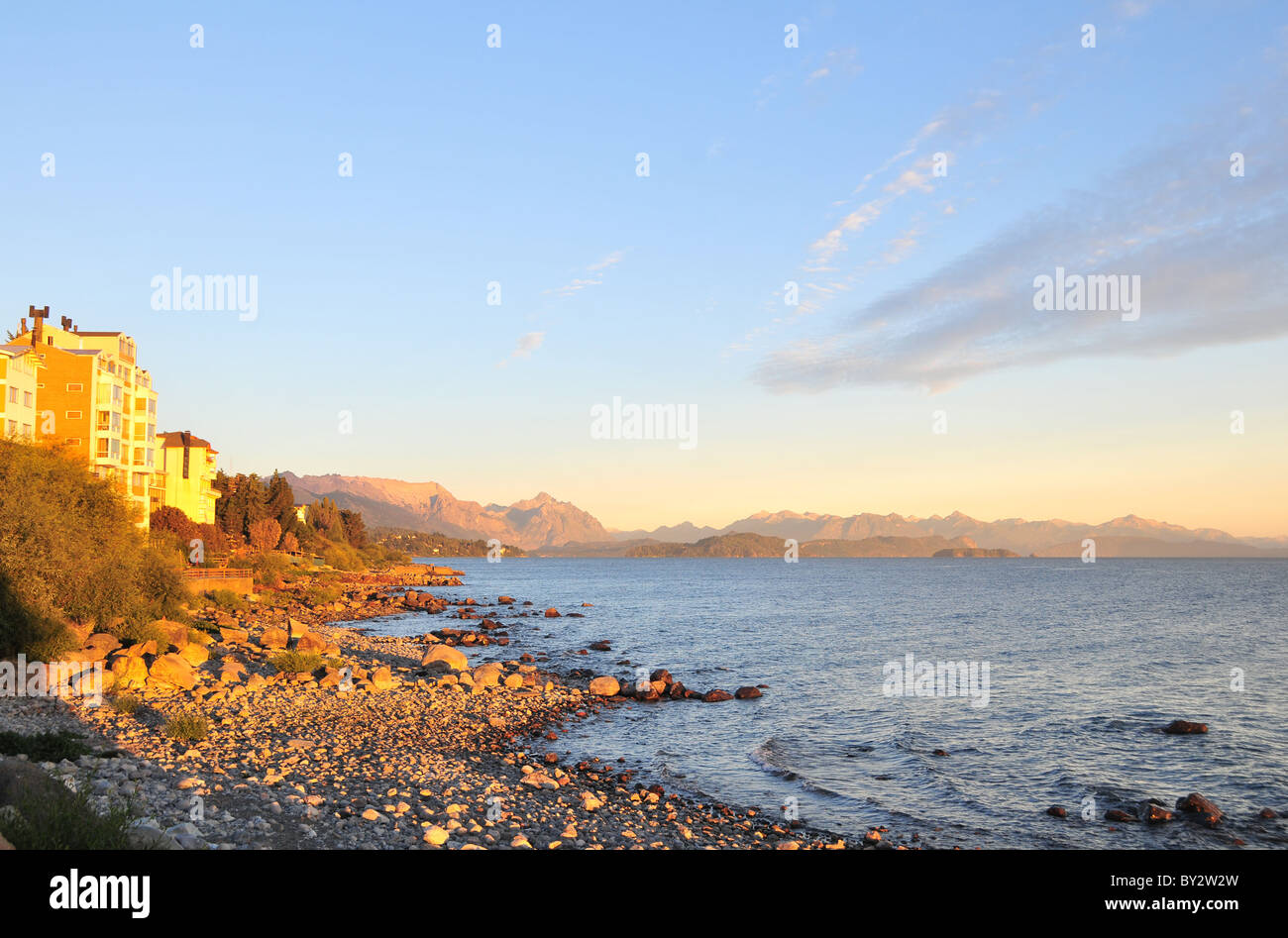 Bright morning sunlight shining on hotels, gravel beach, Lake Nahuel Huapi and Cerro Lopez Andean peaks, Bariloche, Argentina Stock Photo