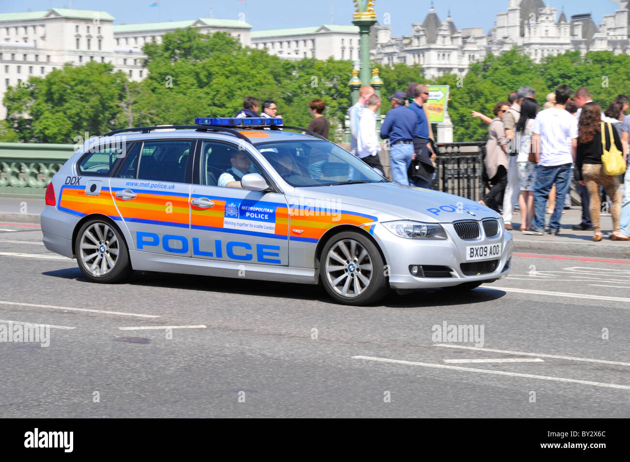 Street scene uniformed officers in Metropolitan Police patrol car driving across Westminster Bridge with group of tourists beyond London England UK Stock Photo