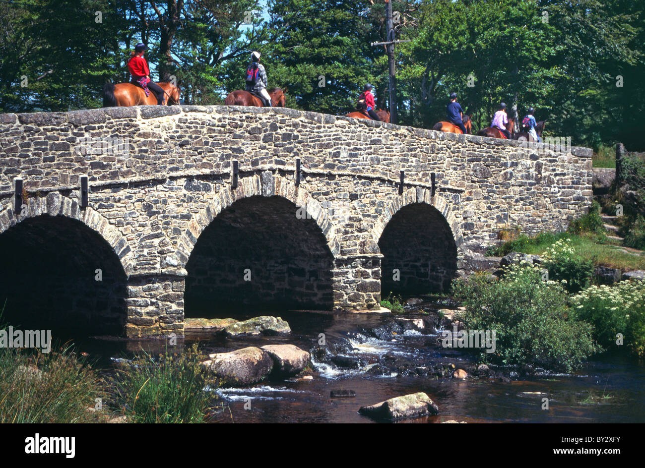Pony trekking over the old stone bridge at Postbridge crossing the East Dart river in the