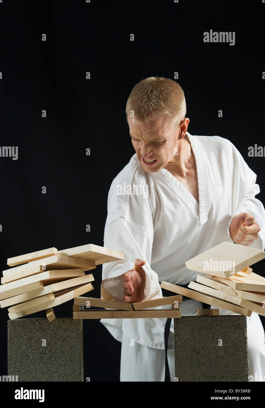 Young Man Breaking Boards With Karate Chop On Black Background Stock