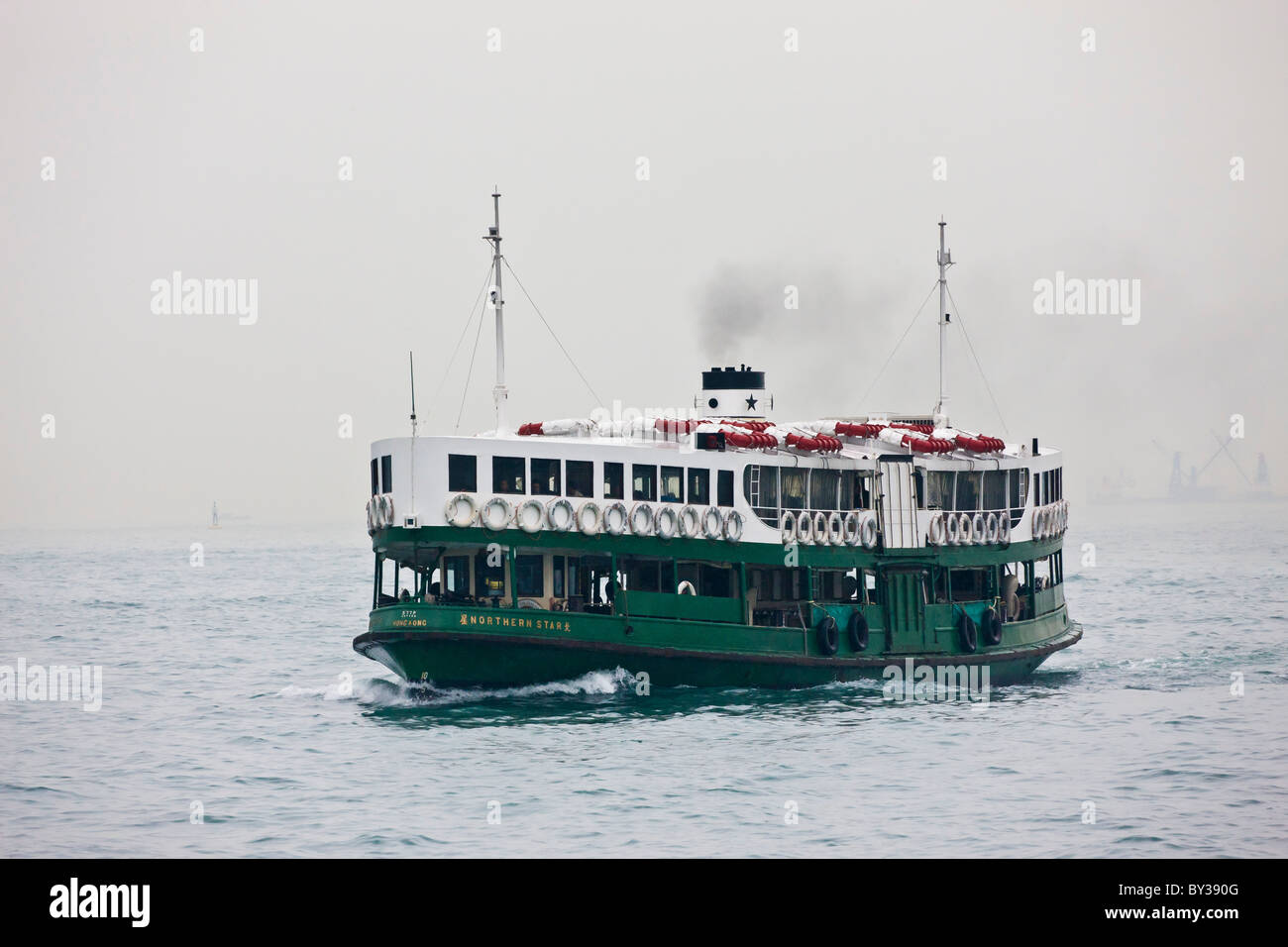 Star Ferry crossing Victoria Harbour between Kowloon and Hong Kong Island on typical hazy day. JMH4138 Stock Photo