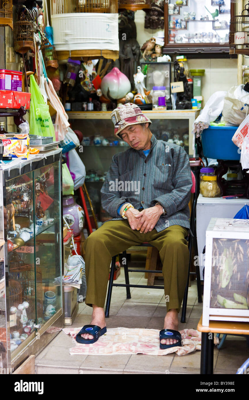 Shop keeper catching a nap in the Bird Market, Yuen Po Street, Nathan Road, Kowloon, Hong Kong. JMH4149 Stock Photo