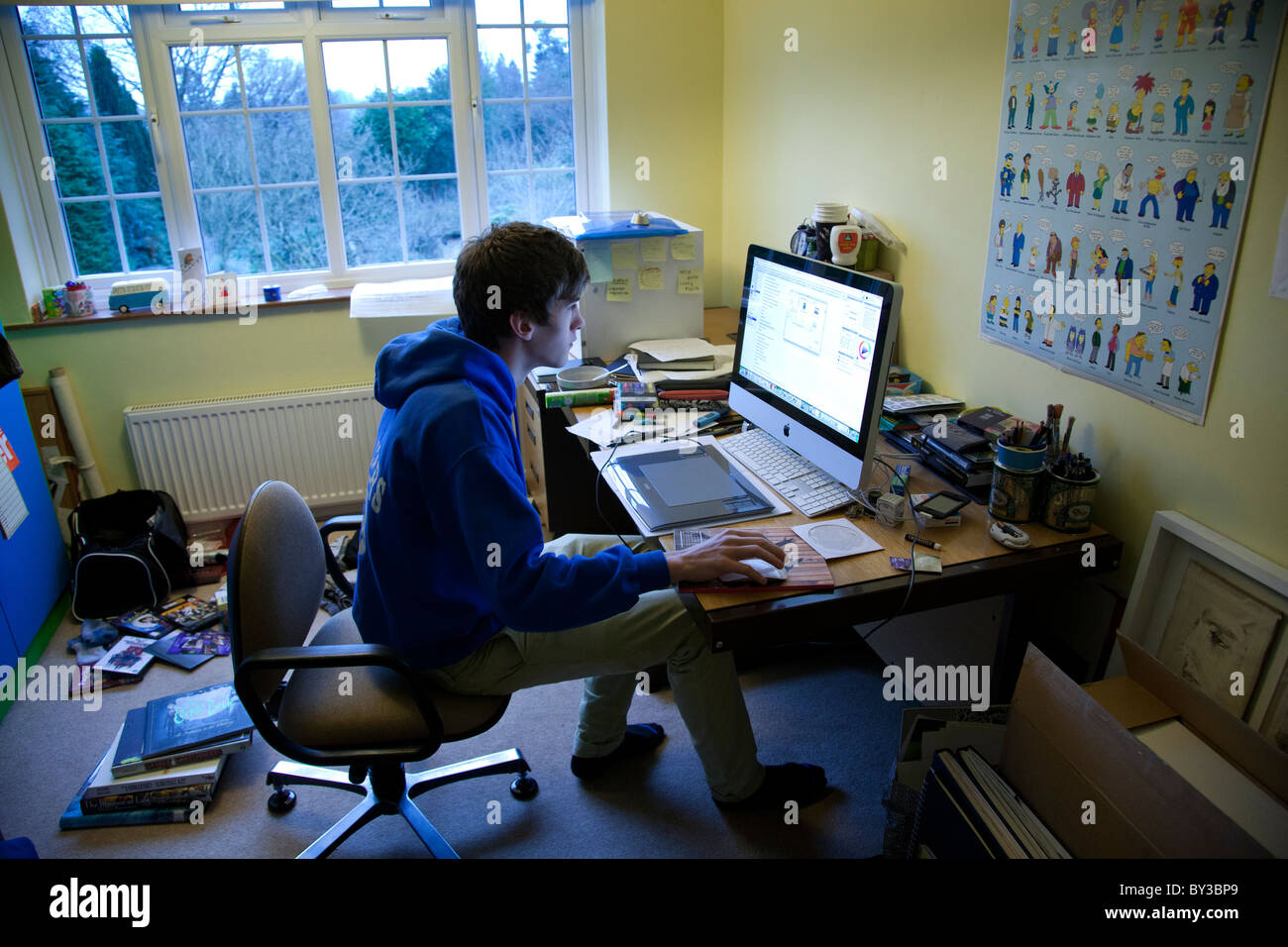 Student working at his desk using an Imac in his untidy bedroom. Stock Photo