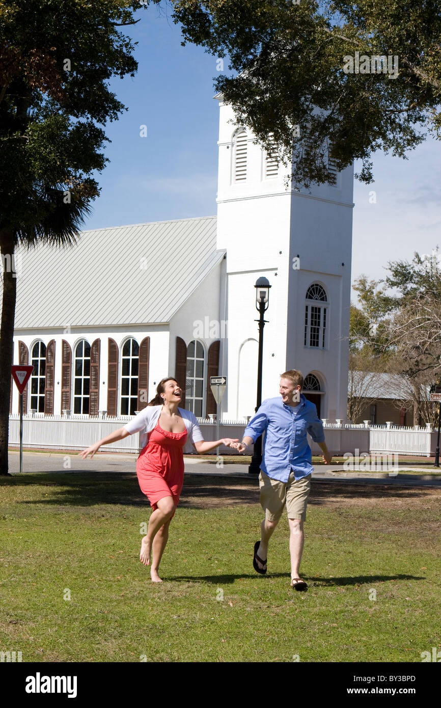 An engaged couple hold hands as they have fun, running by a church. Stock Photo