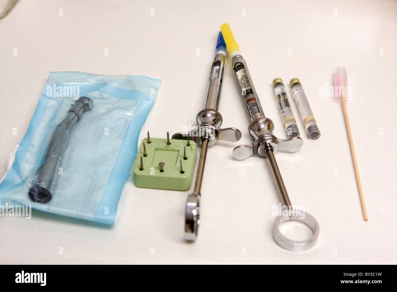 Dental syringes along with a drill and drill bits sit on a tray ready ...