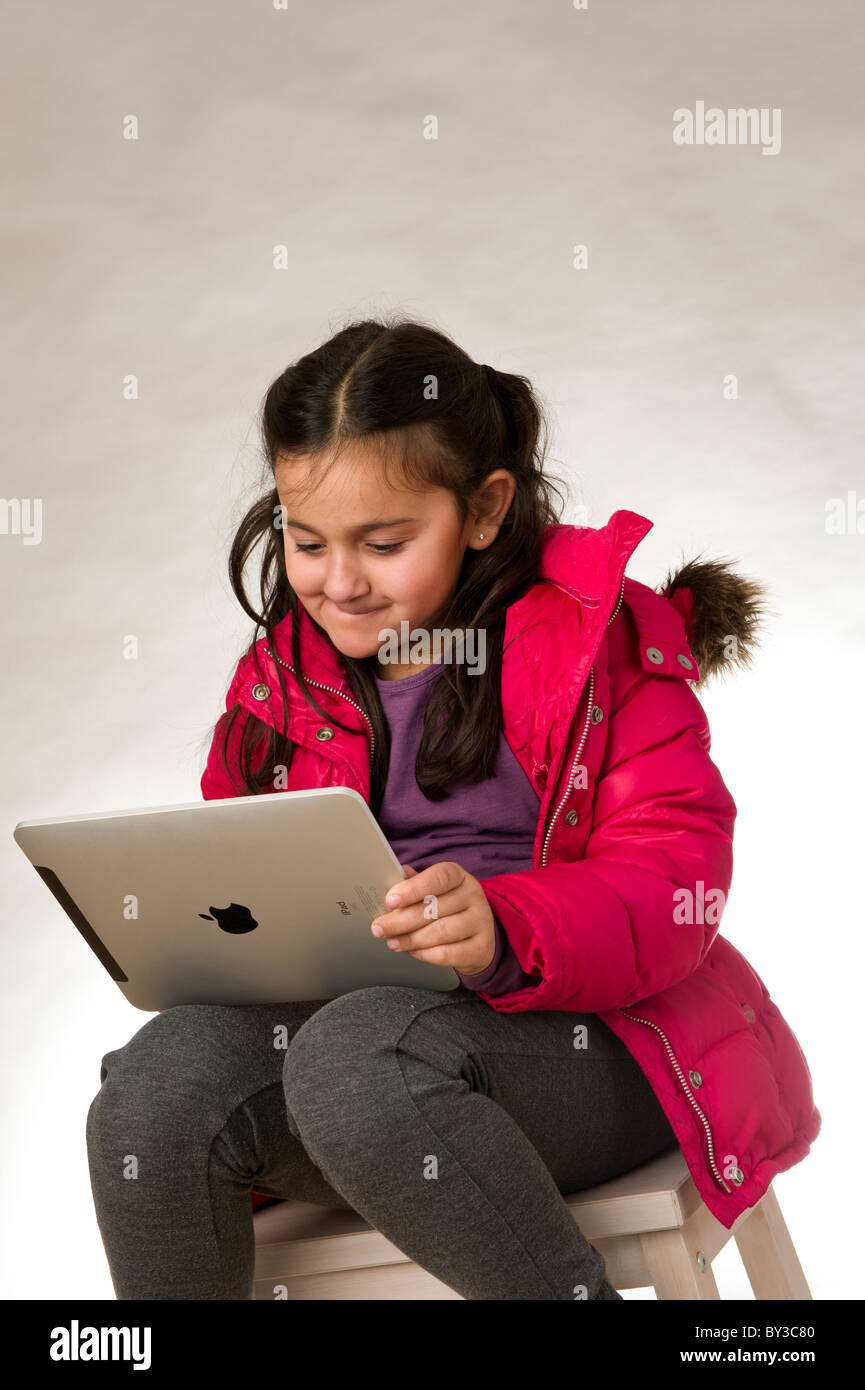 Studio shot of a young girl wearing a red coat and  playing a game on the touch pad screen of an ipad Stock Photo