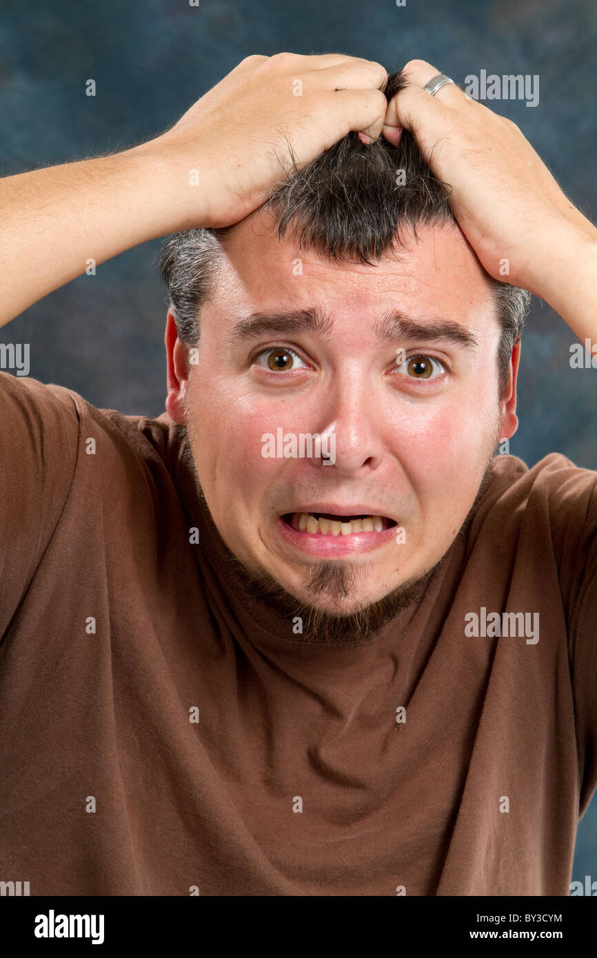 Man in a state of extreme frustration pulls at his hair in response. Stock Photo