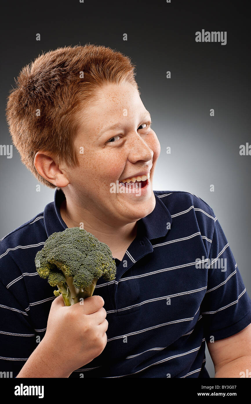 Portrait of redhead teenage boy (14-15) holding broccoli and laughing, studio shot Stock Photo