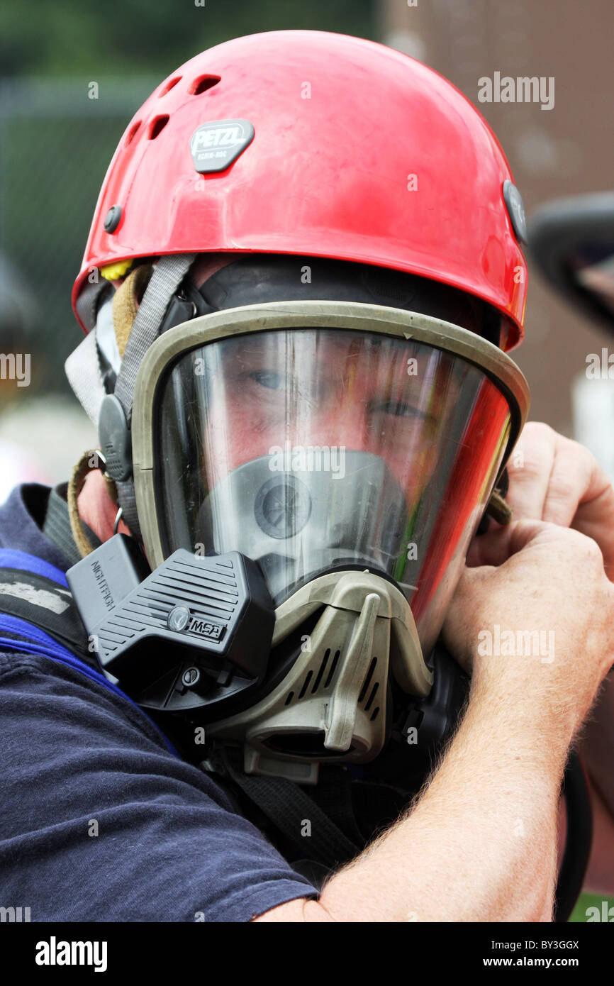 A firefighter putting on a breathing apparatus gear for a hazmat suit at a chemical haz mat spill incident Stock Photo
