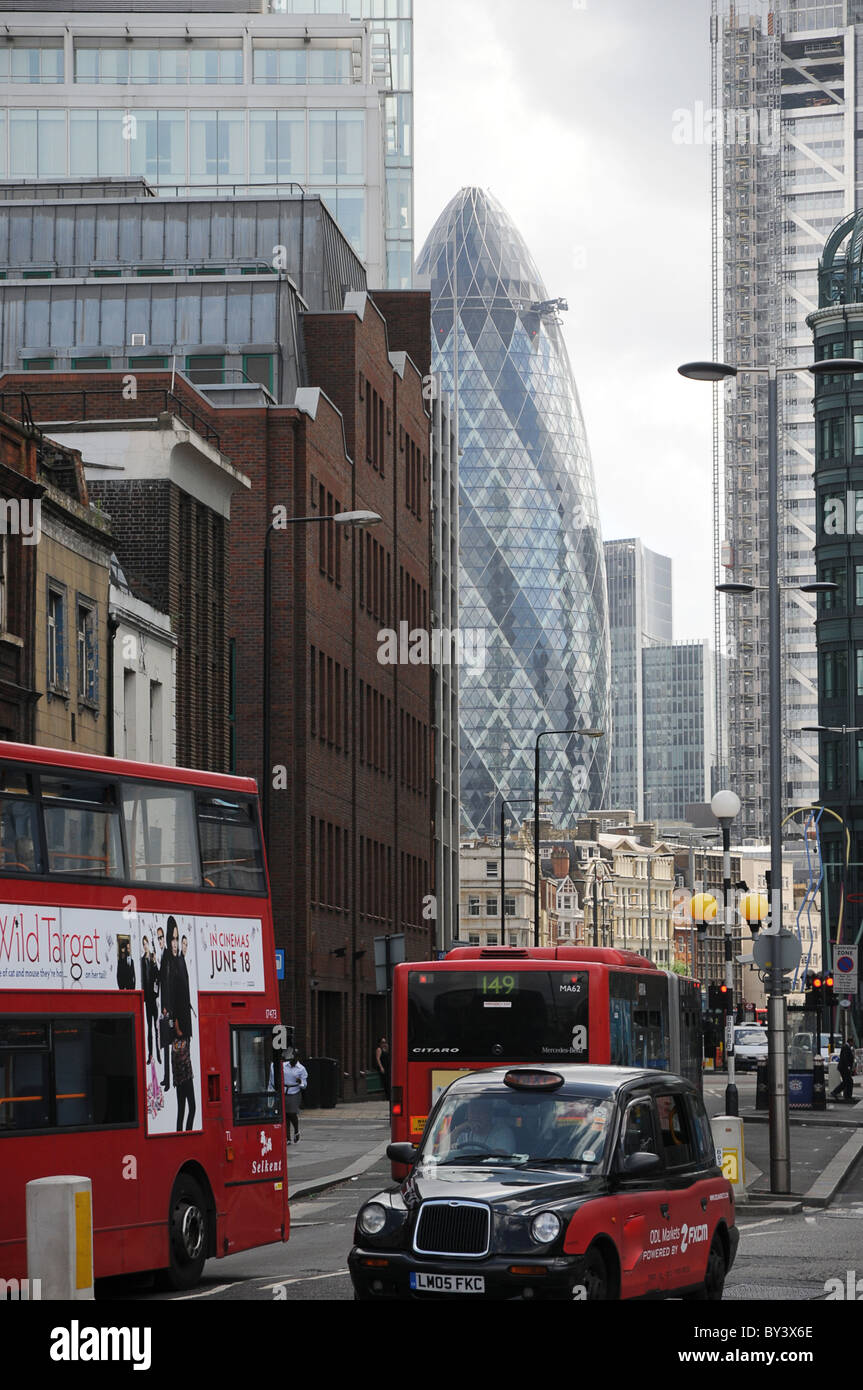 A vertical shot of the Gherkin building and neighboring buildings in London with a double decker bus in the foreground. Stock Photo