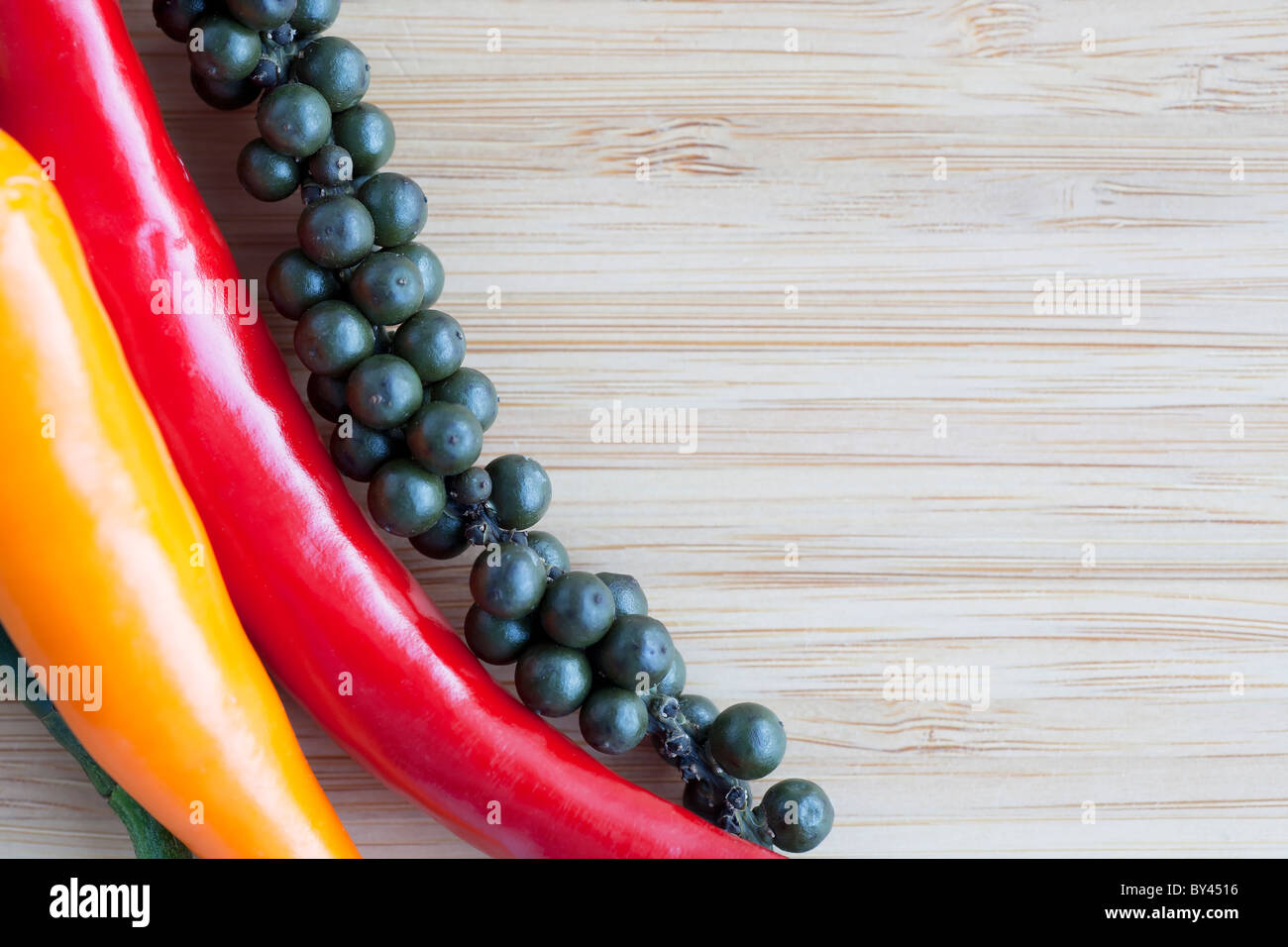 Red and orange hot peppers and fresh on the stalk pepper corns on wooden surface with copy space. Stock Photo