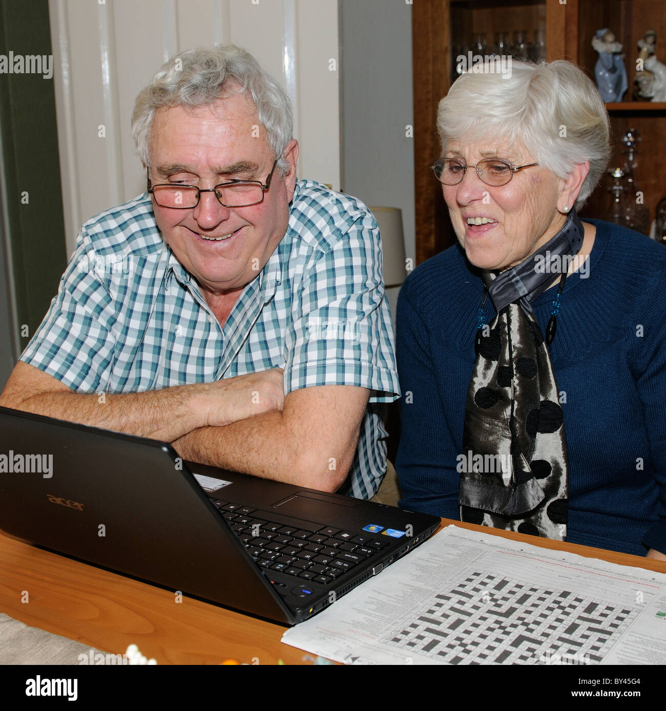 Elderly couple using their laptop to Skype friends over the internet from their lounge Stock Photo