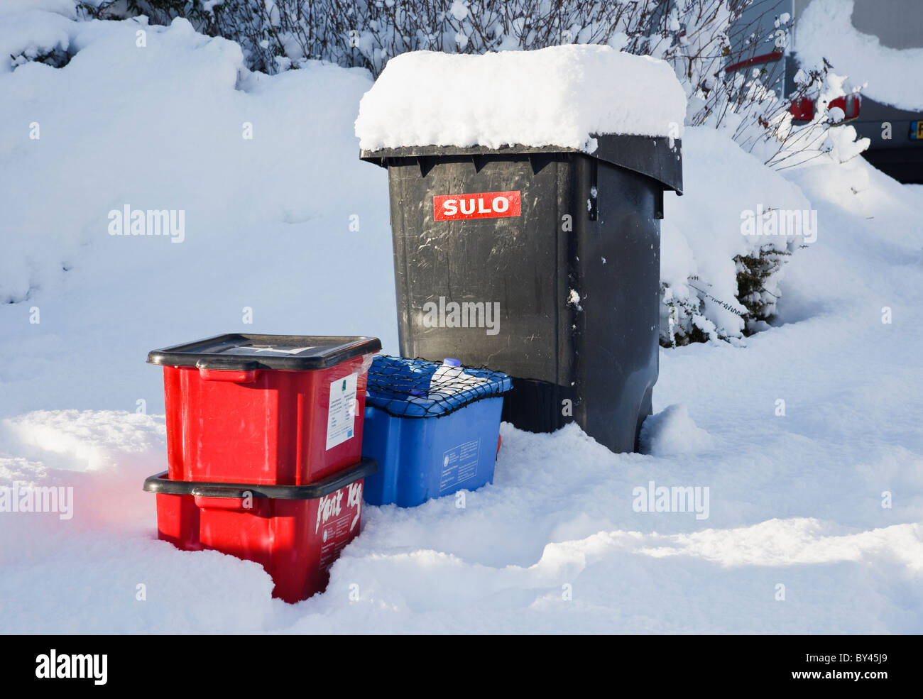 Wheelie bin and kerbside recycling boxes awaiting collection outside in the snow. UK, Britain. Stock Photo