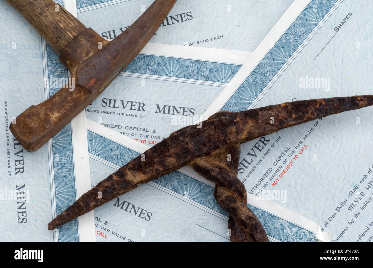 Two old mining picks resting on silver mine stock certificates. Stock Photo