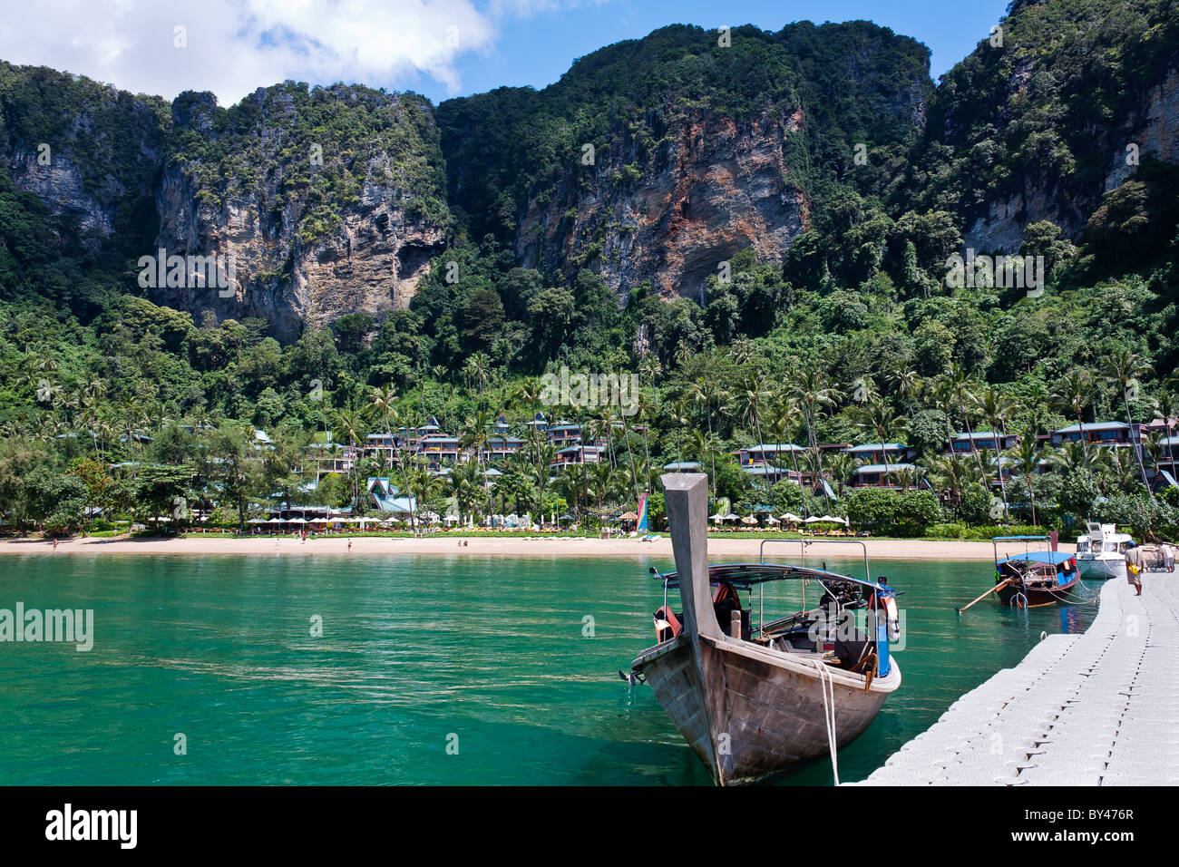 A Longtail boat moored at a pontoon with beach and rain forest in the background Stock Photo