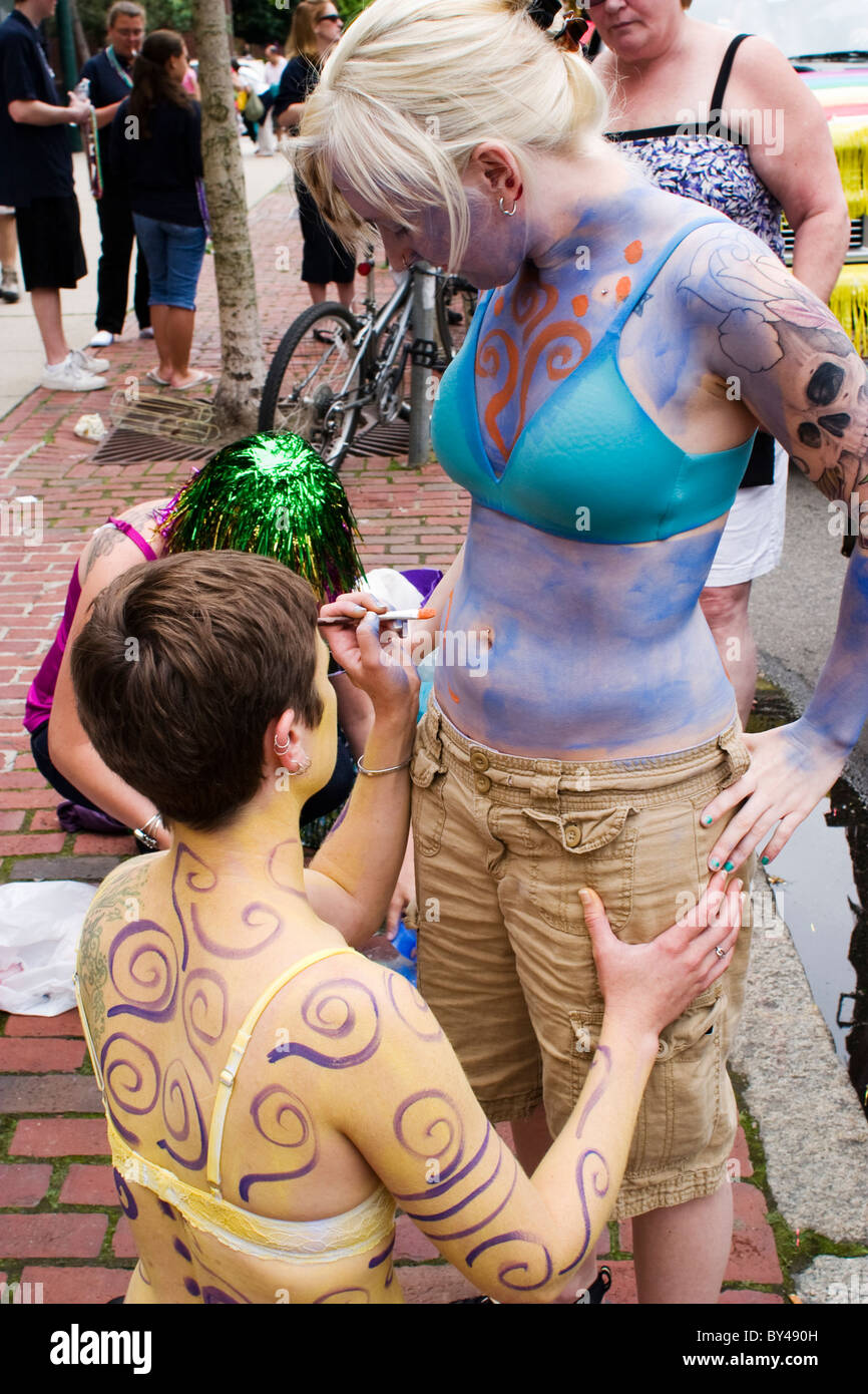 Two tattooed and pierced lesbians paint their bodies in front of a float preparing for Boston's Gay Pride March. Stock Photo