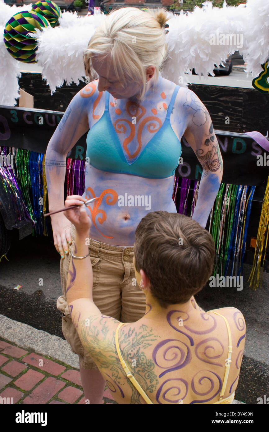 Two tattooed lesbians paint their bodies in front of a float, preparing for Boston's Gay Pride March. Stock Photo