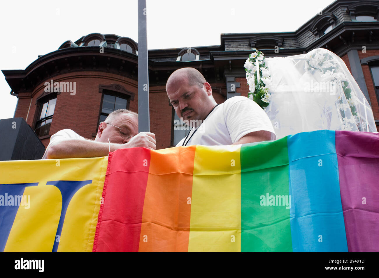 Two gay men attach a rainbow flag to their float for the Boston Gay Pride March in the South End staging area. Stock Photo