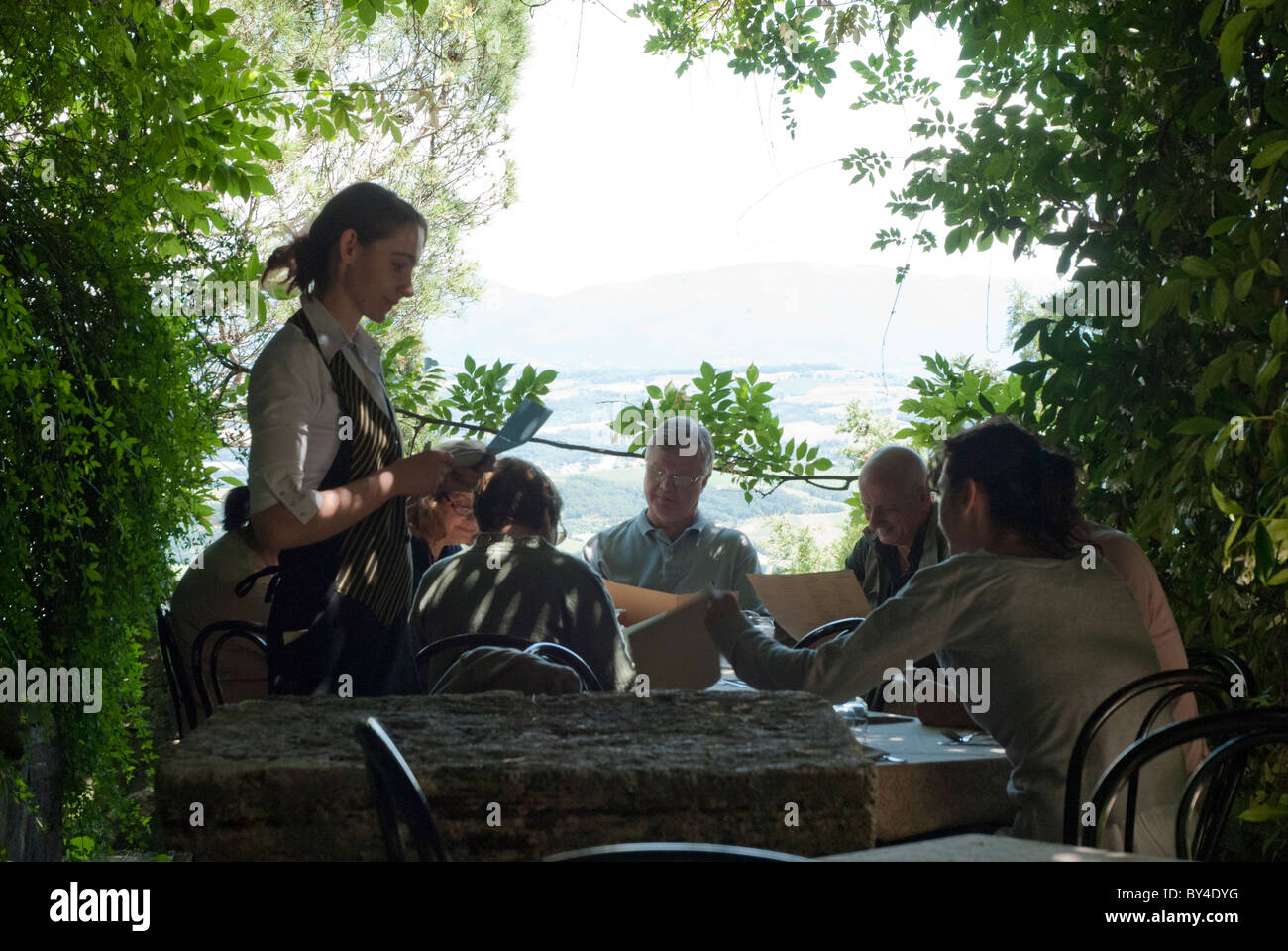 customers seated at restaurant table under shade of plant arch with view and waitress taking order Stock Photo