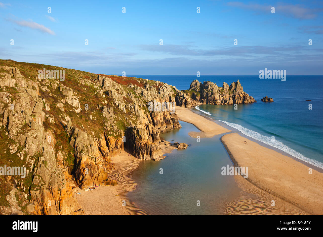 Large tidal pool covers the beach as the evening sun filters through bathing Logan Rock in warm sunshine, Porthcurno Stock Photo