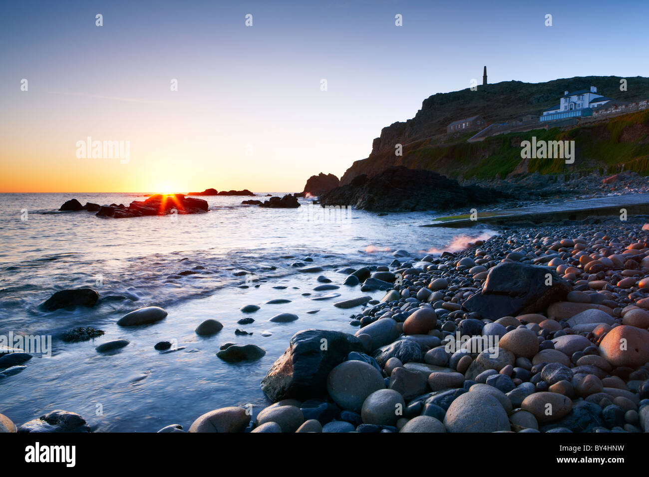 A clear evening sky and the last rays of sunlight highlight the small rocky beach at Priest's Cove Cape Cornwall Stock Photo