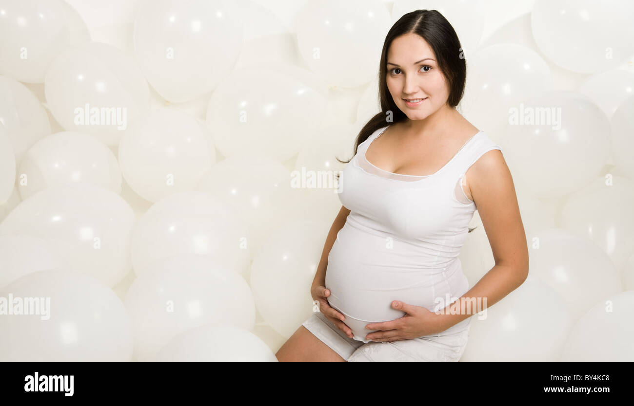 Photo of pregnant woman in casual clothes sitting inside white balloons Stock Photo