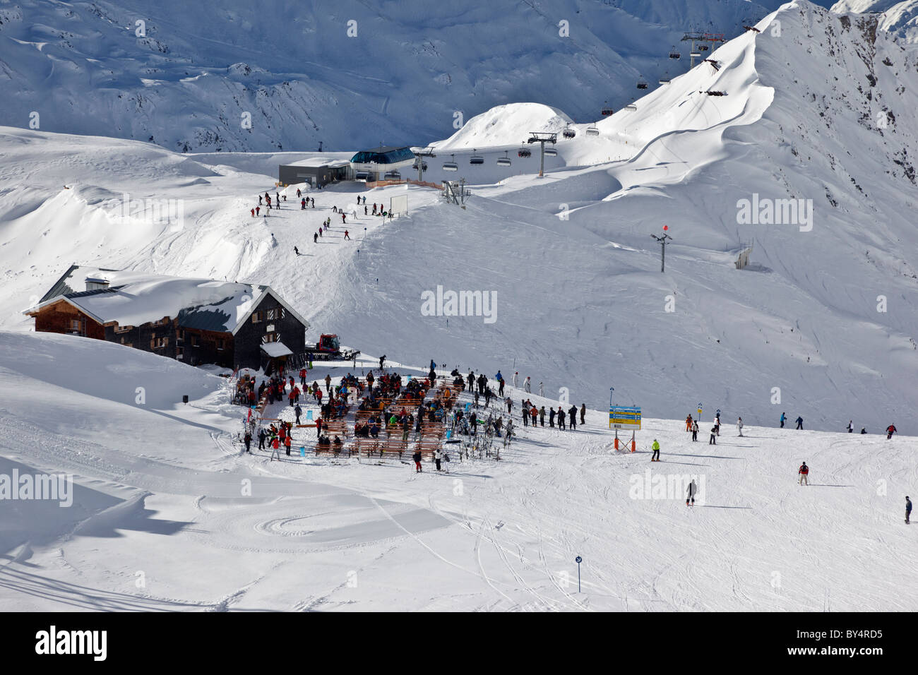 Skiers and snowboarders stop for a break at the famous Ulmer Hutte in St Anton.  The Valfagehr chairlift is in the distance. Stock Photo
