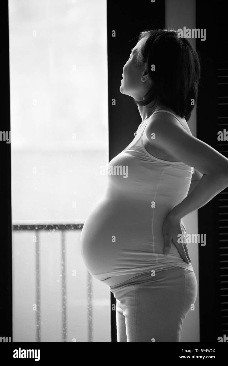 Pregnant lady looking away to outside home, made in black and white. PS : there might be noticable noise by high ISO setting Stock Photo