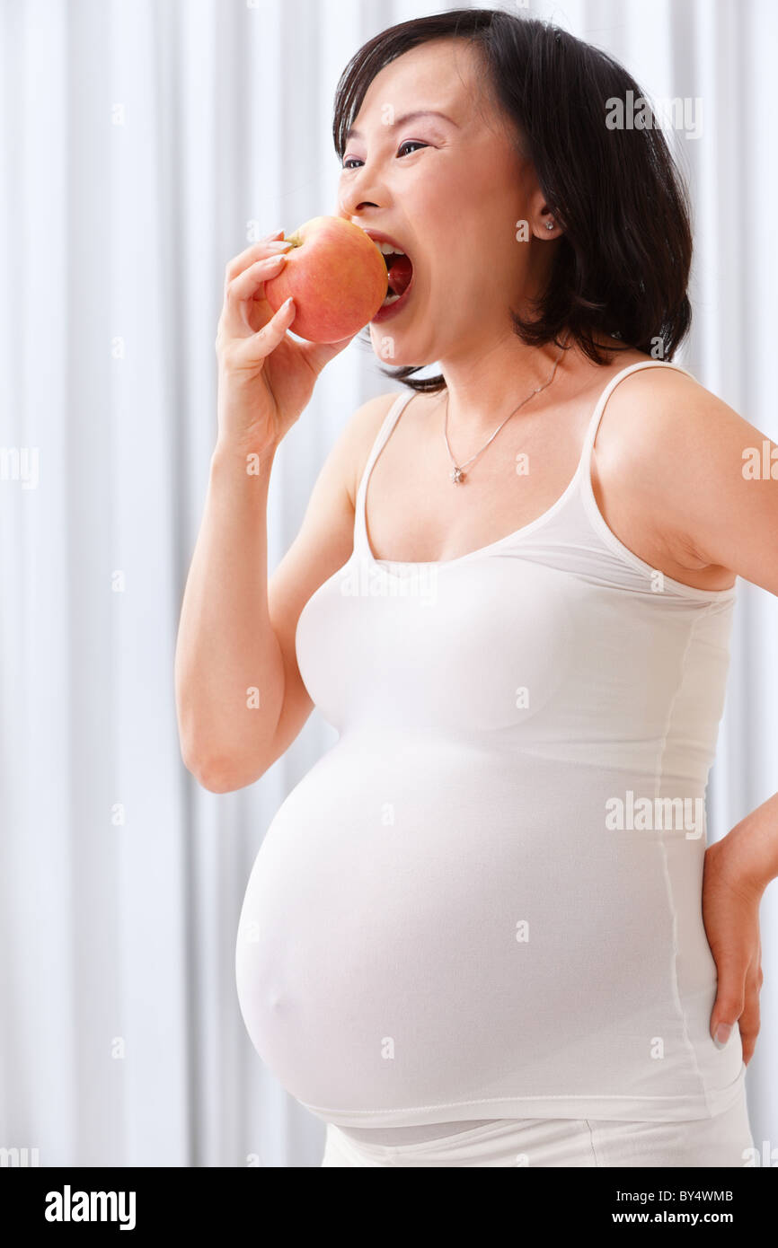 Asian pregnant lady eating an apple, with white attire Stock Photo