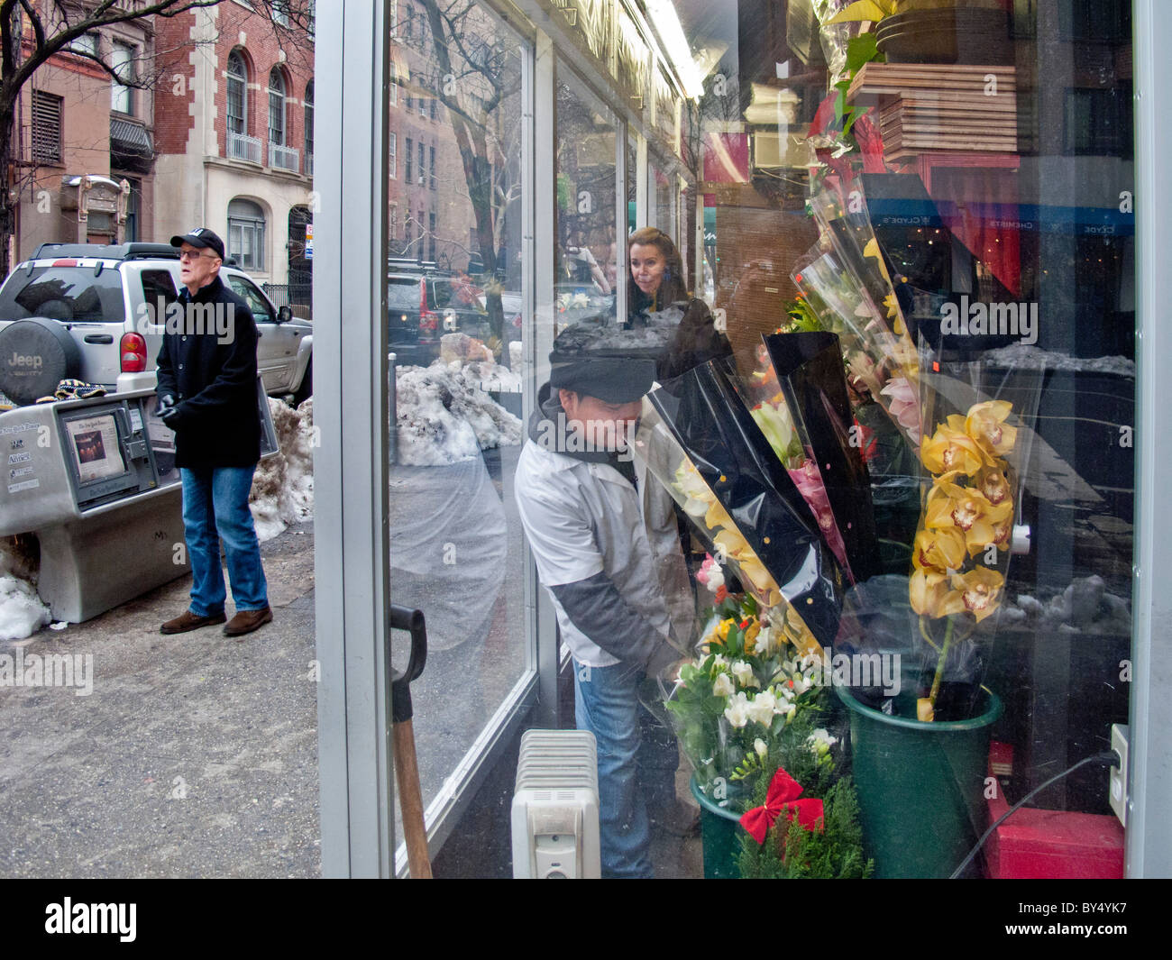 While her husband searchers for a taxi, a woman purchases fresh flowers at a warmed sidewalk kiosk on a winter day in NYC. Stock Photo