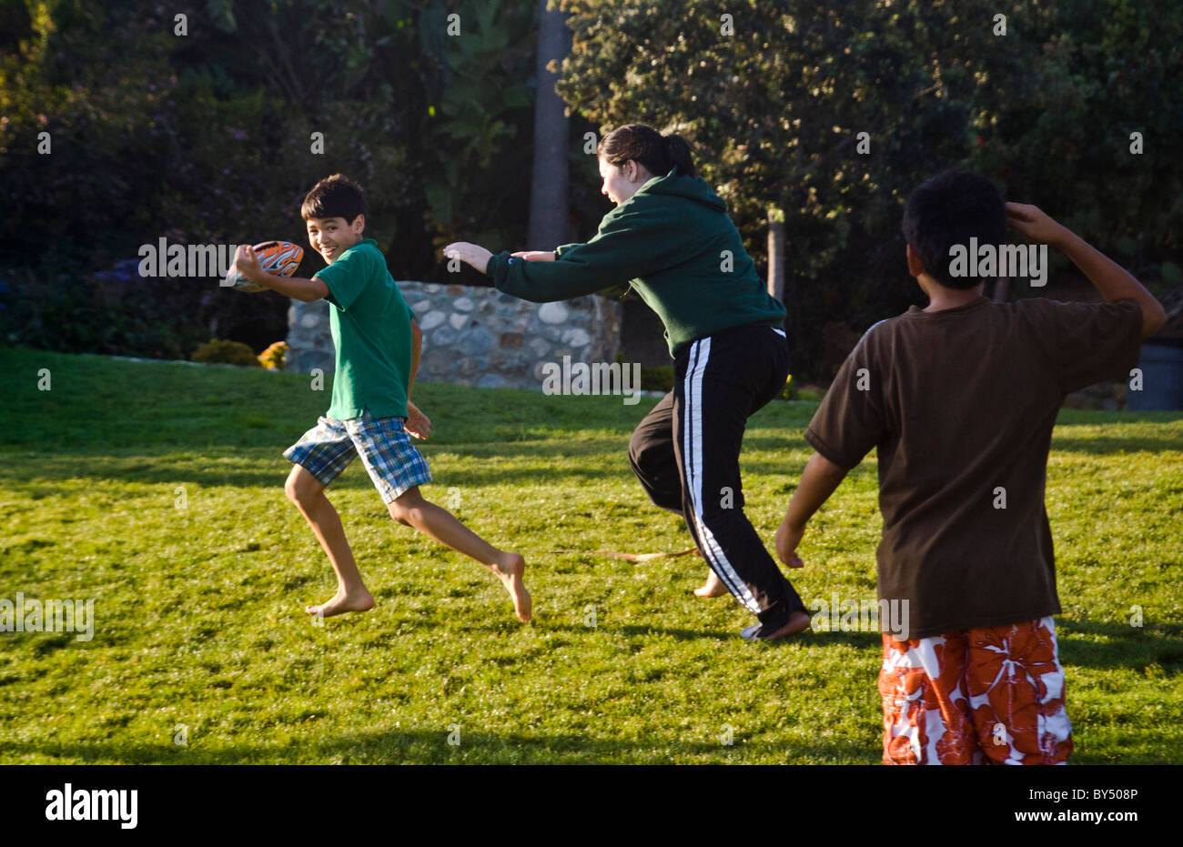 An Asian-American teenager plays touch football with her brother in afternoon sun in Laguna Beach, CA. MODEL RELEASE Stock Photo