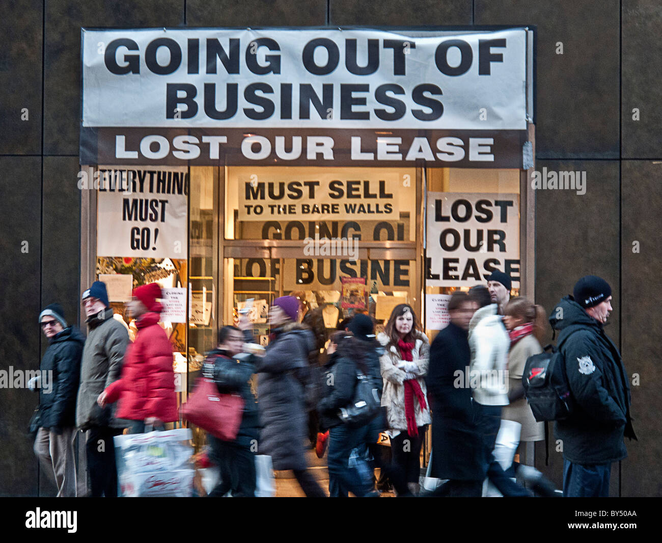 Winter dressed pedestrians walk past a store offering a Going Out of Business sale on Fifth Avenue in Manhattan, New York City. Stock Photo